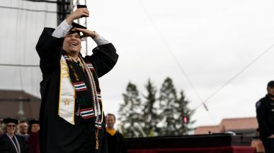 Riley Ofrecio takes a photo of himself with a phone while on the commencement stage.