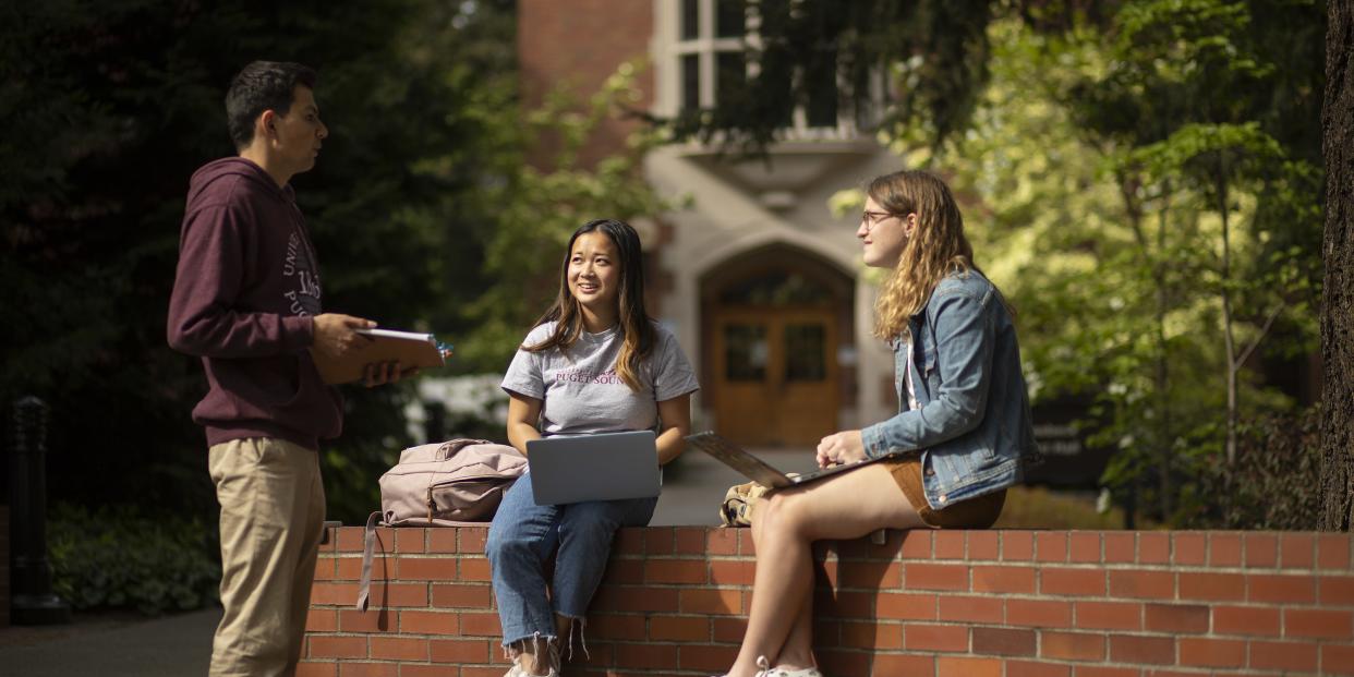 Three students chat outside the science center and music buildings.