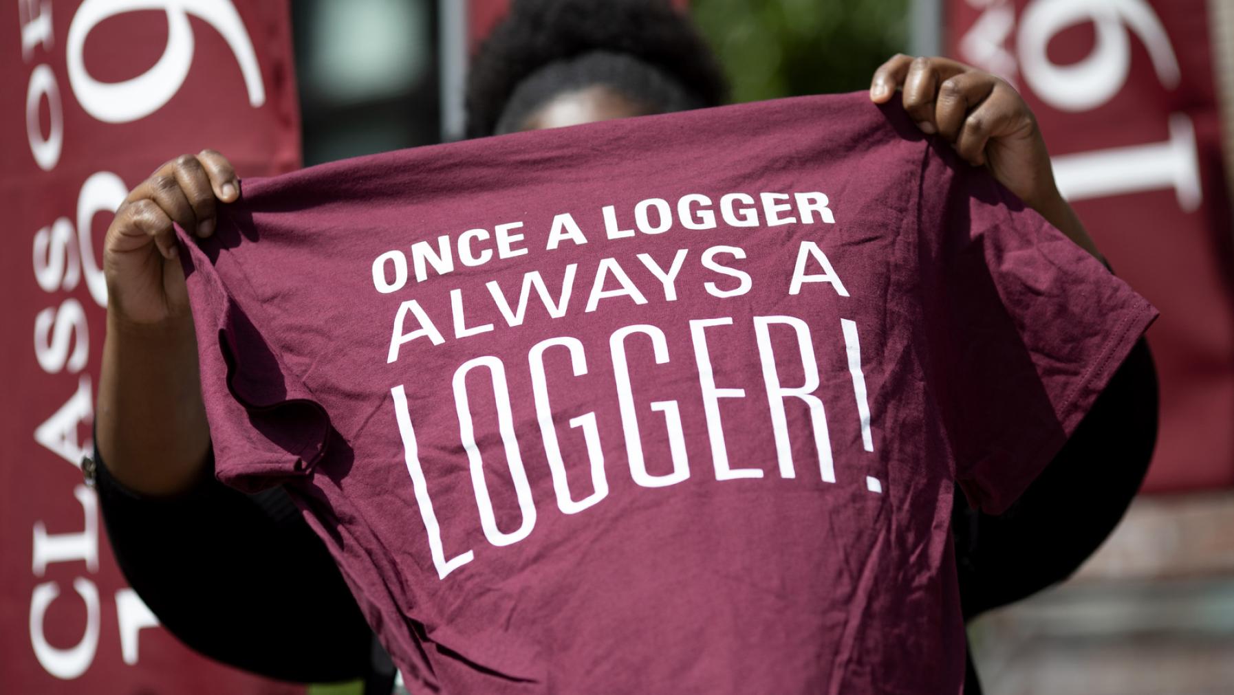 Student holding up a maroon t-shirt that says Once a Logger, Always a Logger!