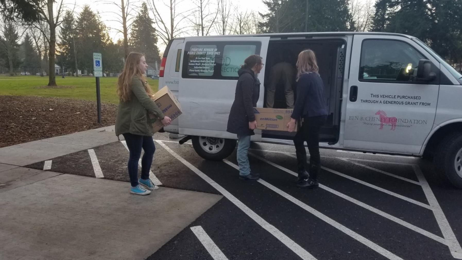 Four people moving some boxes into a van.