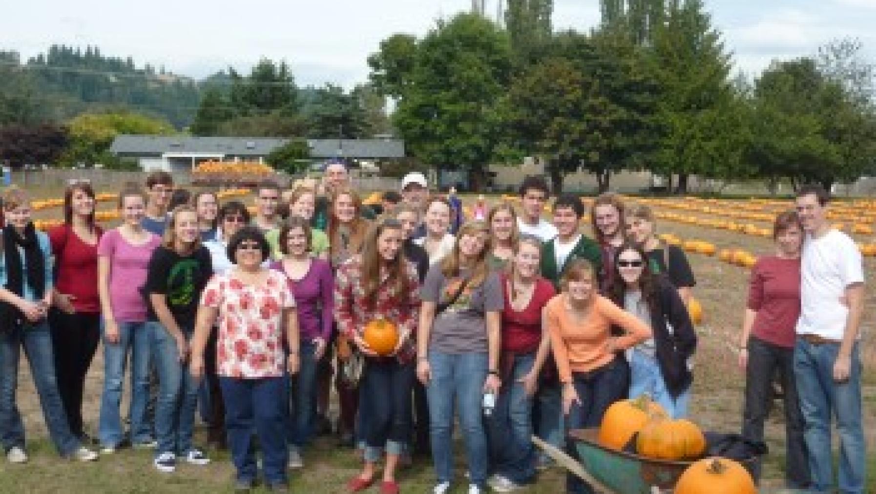 A group of people standing together in front of some pumpkins.