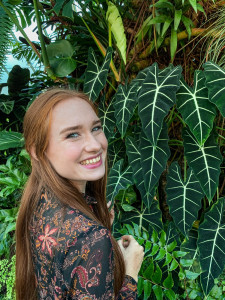 Student smiling at the camera while standing in front of plants