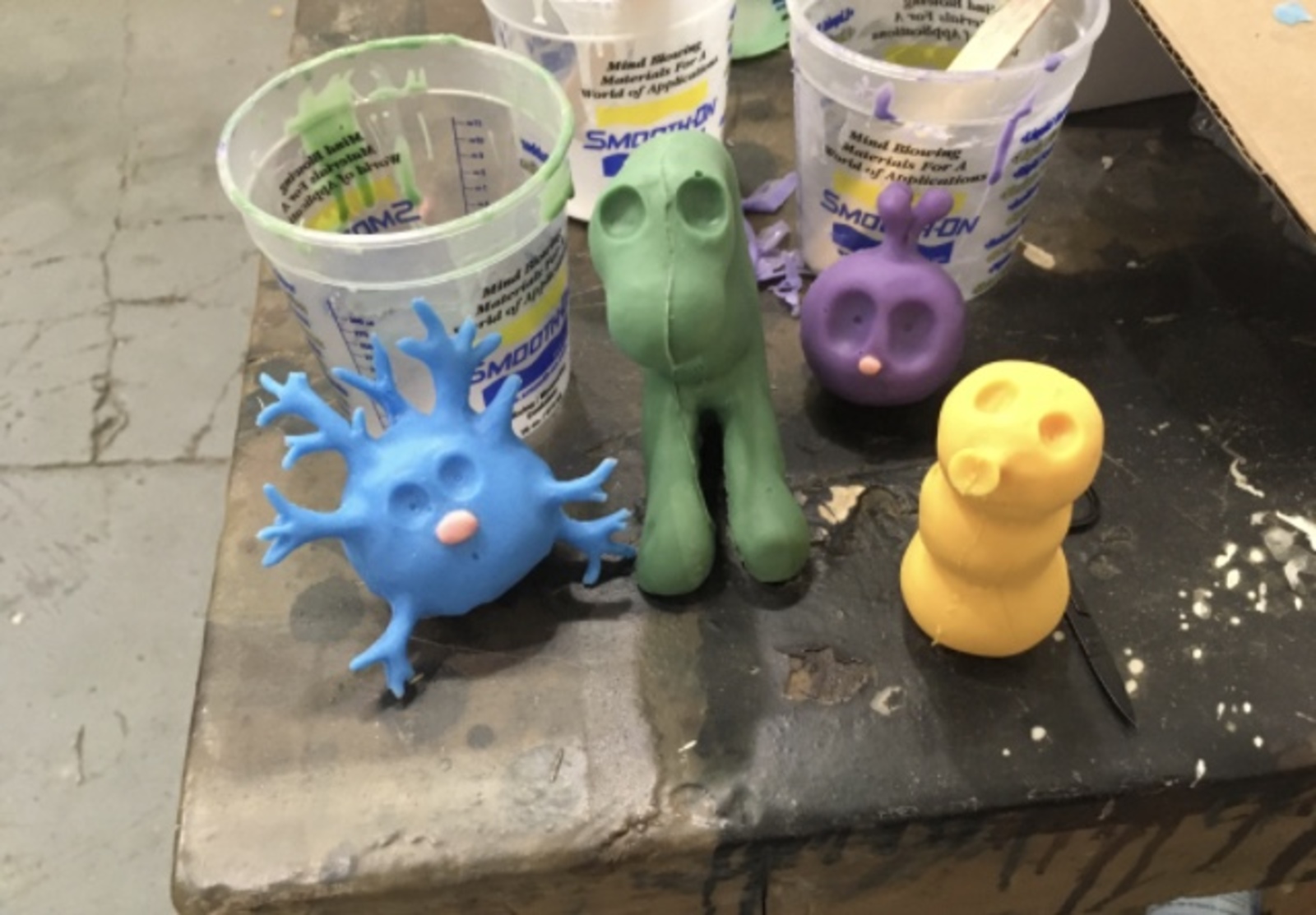 Blue, green, purple, and yellow claymation figures sit on the corner of a work table