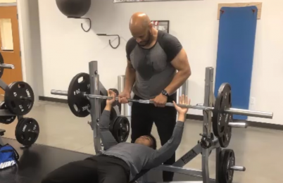Shawn Frank assists a person lifting weights in a gym