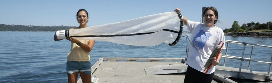 Two students with a long net in front of Puget Sound water.