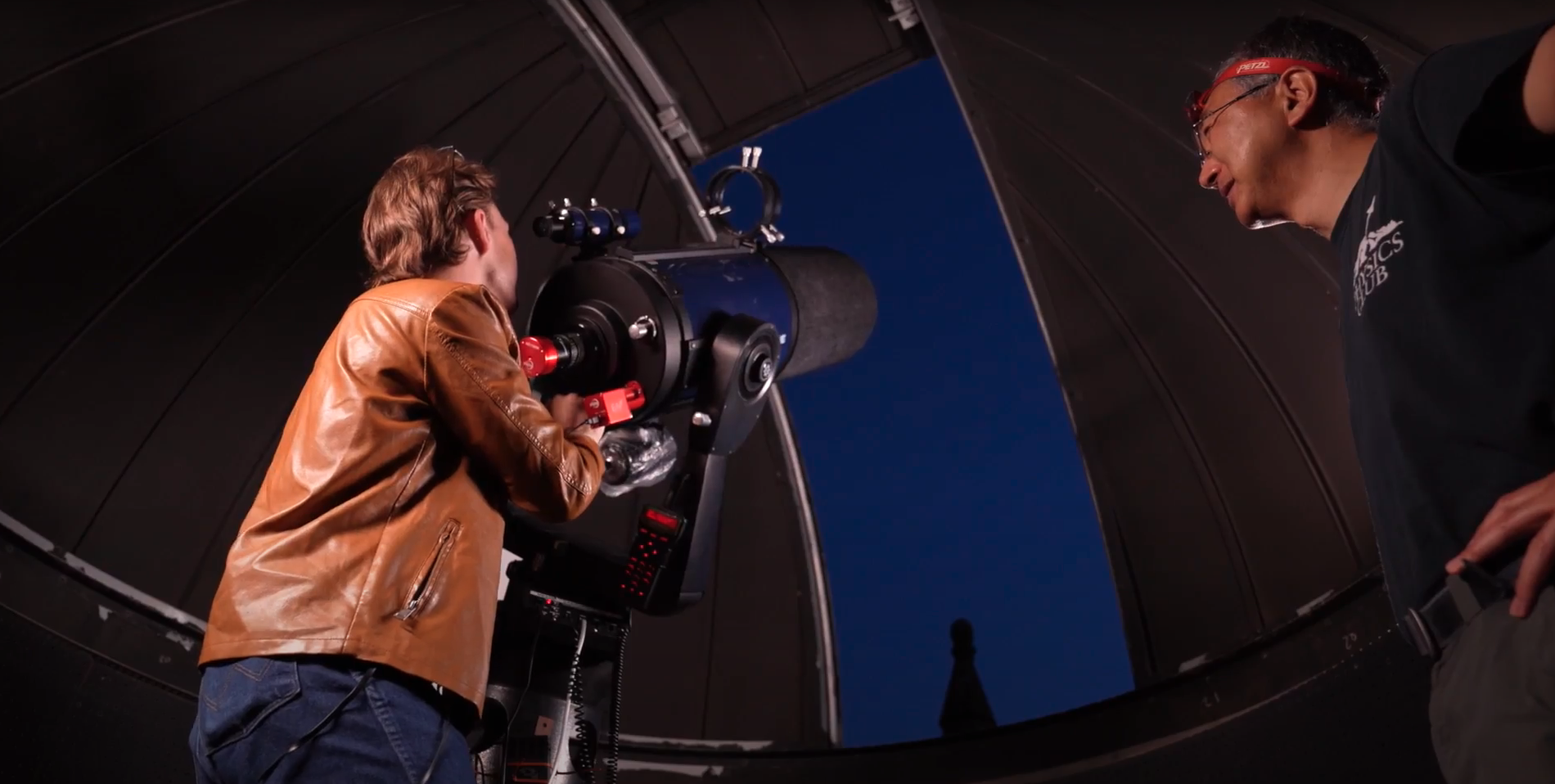 Austin Glock and Visiting Asst. Prof. Tanaka look up past the telescope into the starry sky outside the observatory dome.
