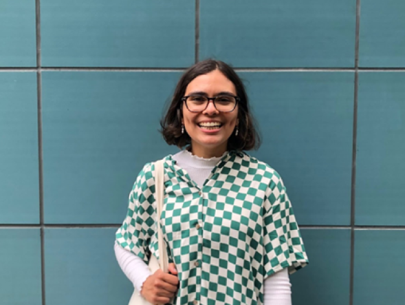 Student Laura Arcia standing in front of a blue wall while smiling at the camera.