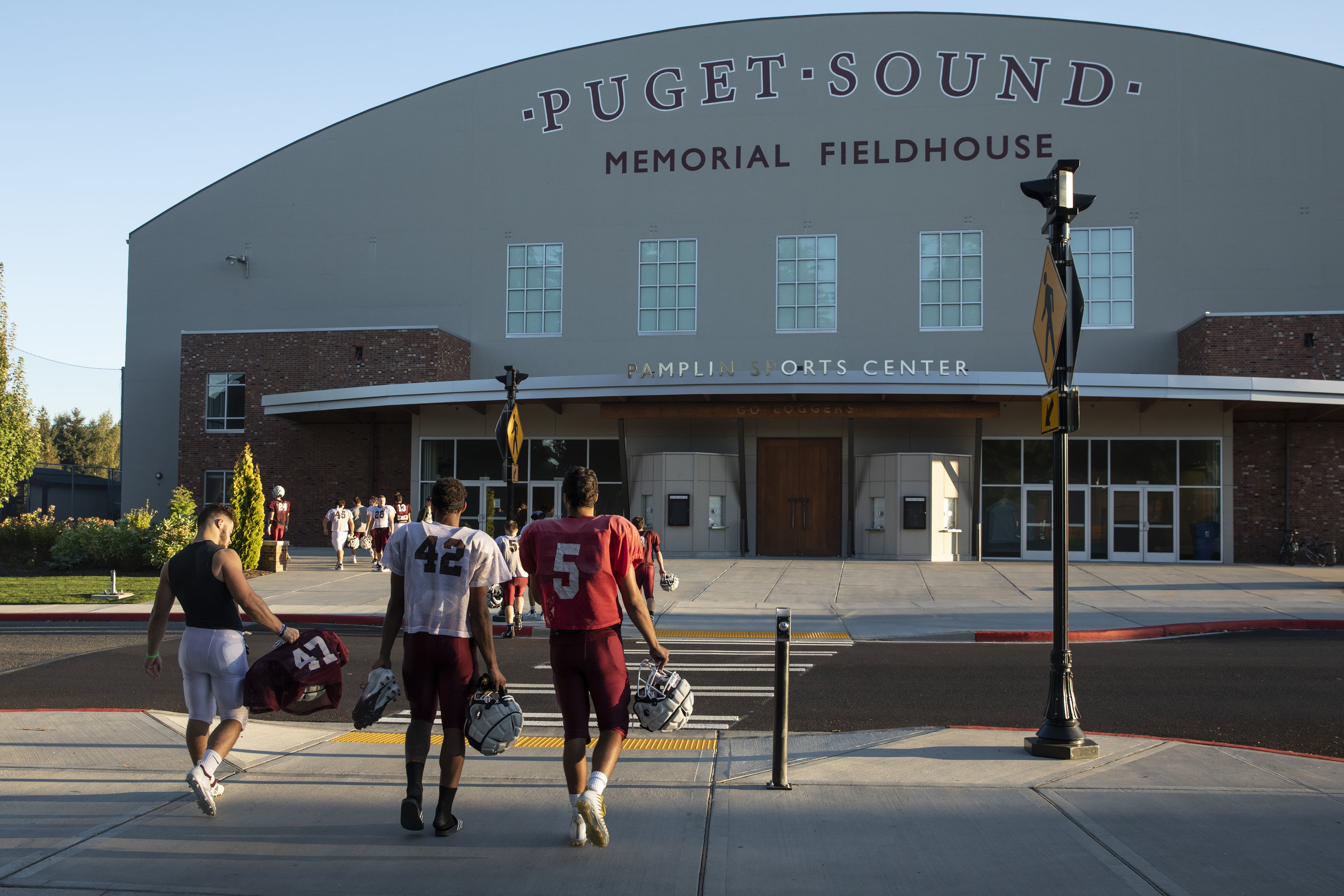 Student-athletes in football gear walk toward Memorial Fieldhouse.