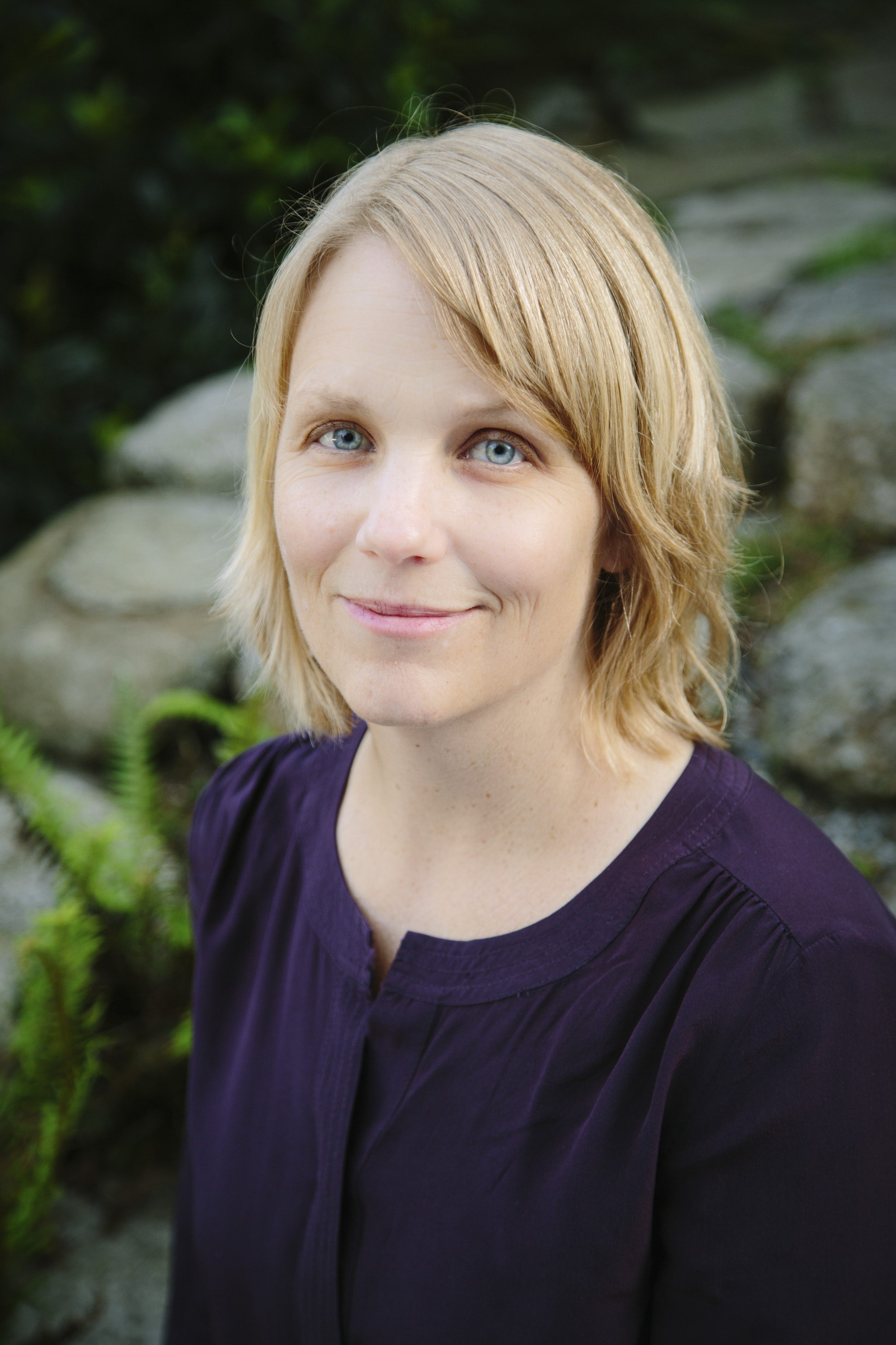 Tanya Erzen is smiling facing the camera in a purple blouse. 