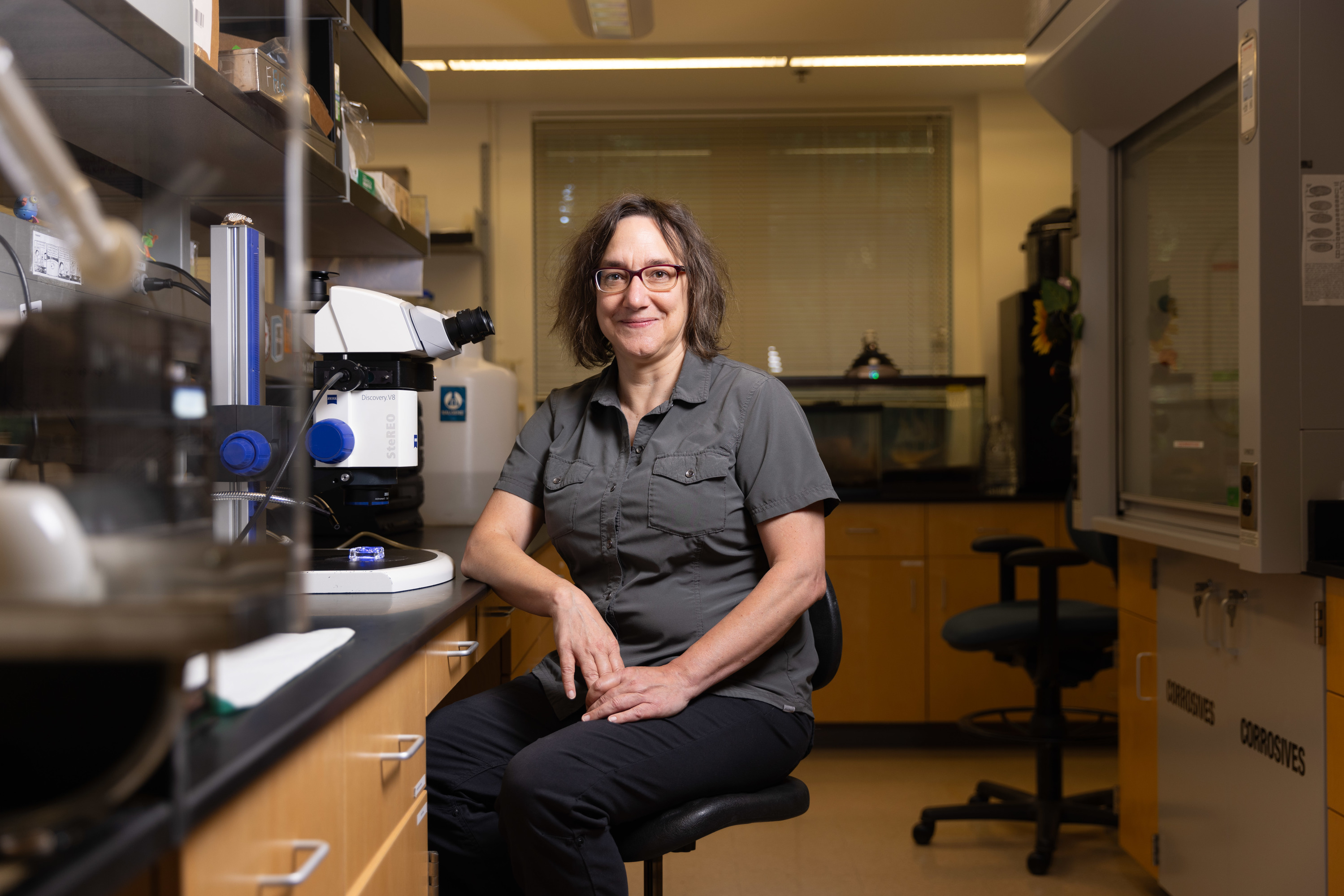 Professor of Biology Leslie Saucedo sits beside a microscope in her lab.