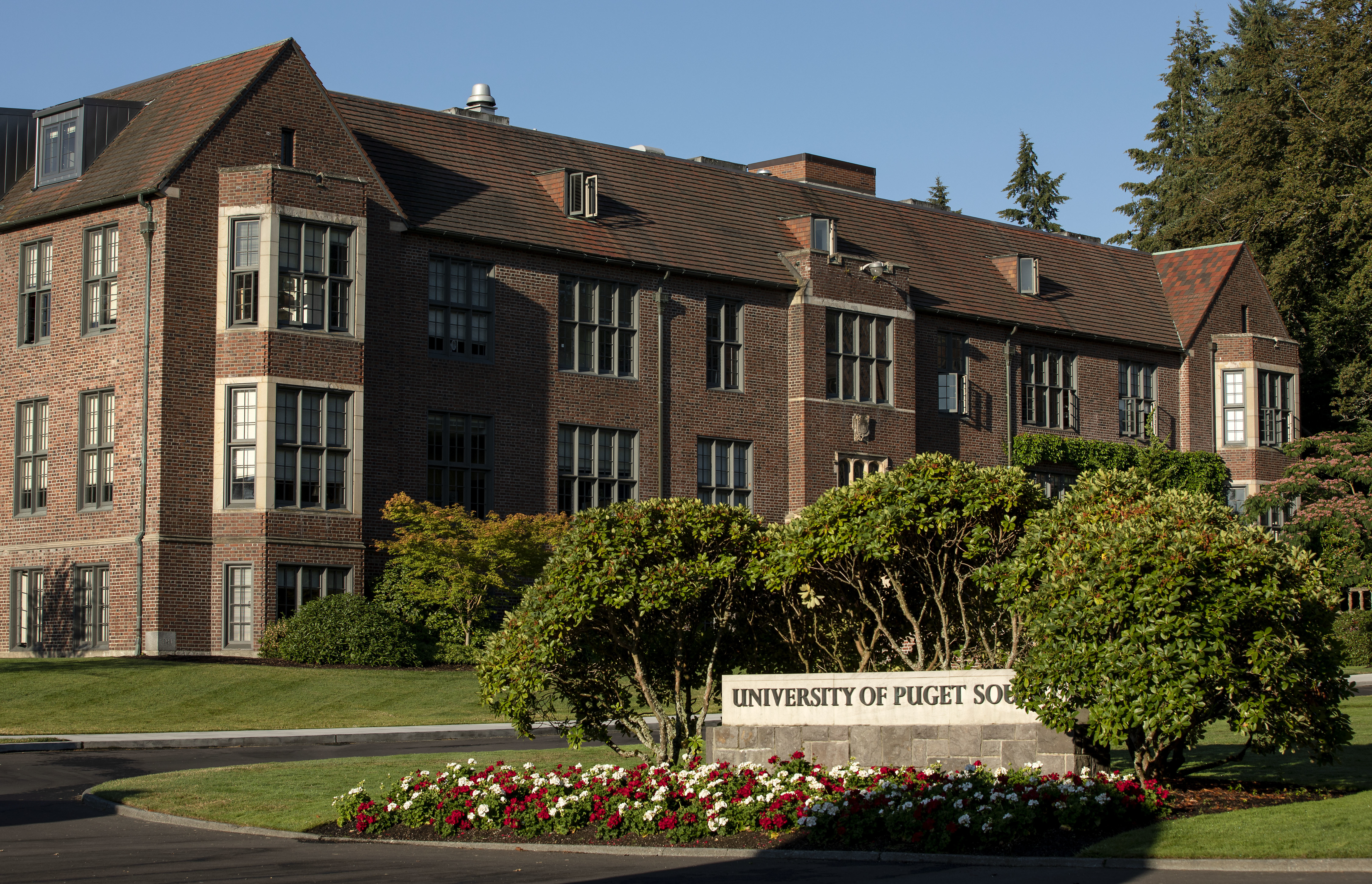 The University of Puget Sound sign sits behind flowers in front of a brick building. 