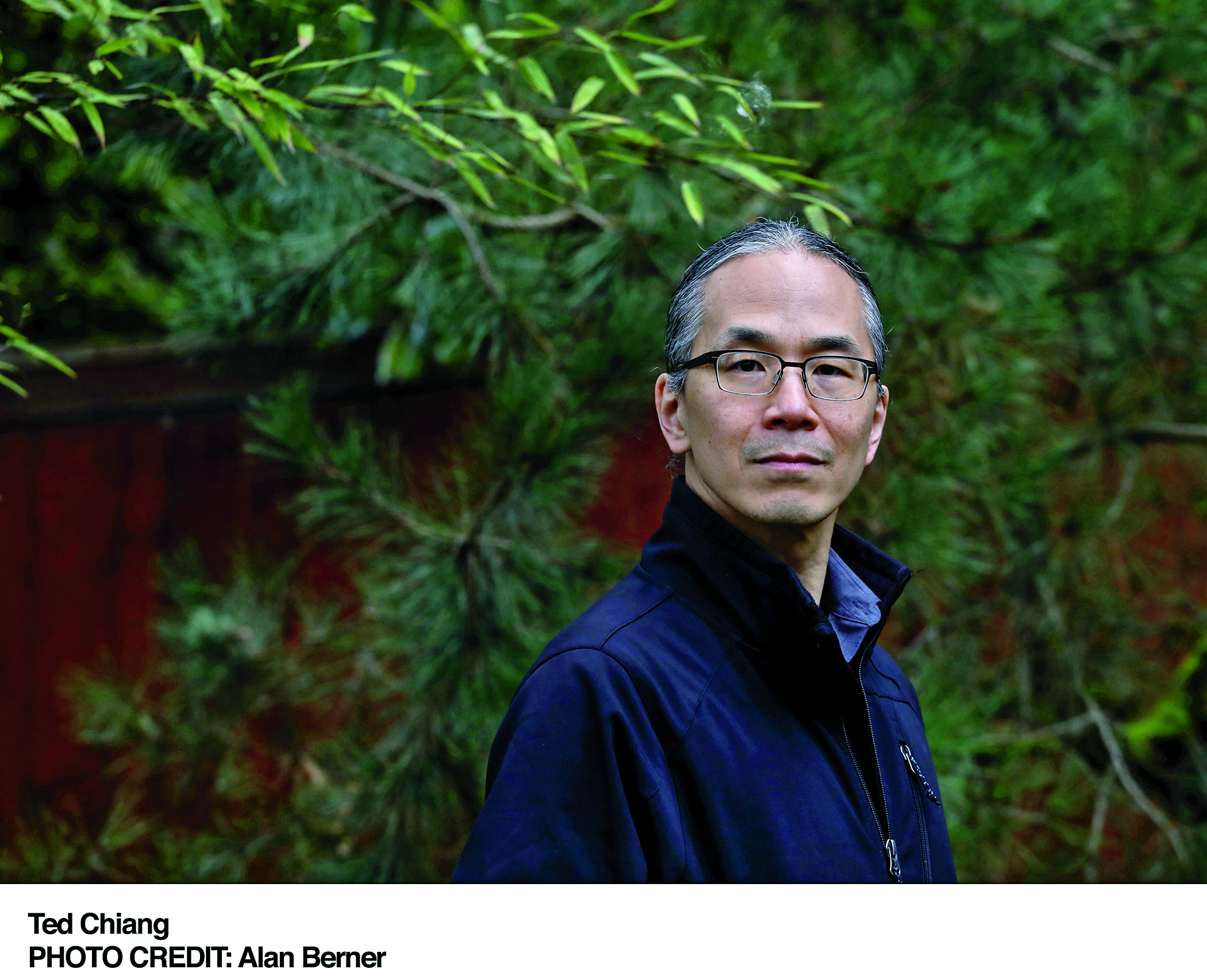 Ted Chiang looks over his shoulder at the camera. He is wearing glasses and a blue coat. 