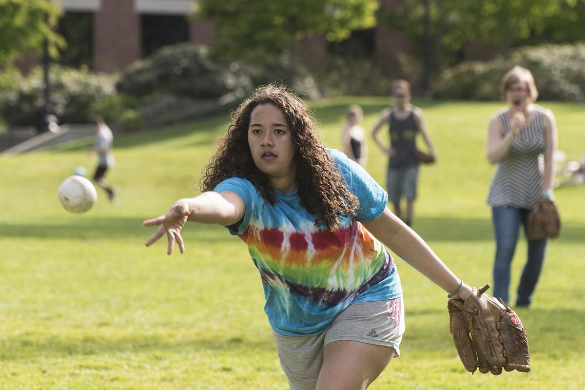 Person pitching a softball with other players standing behind