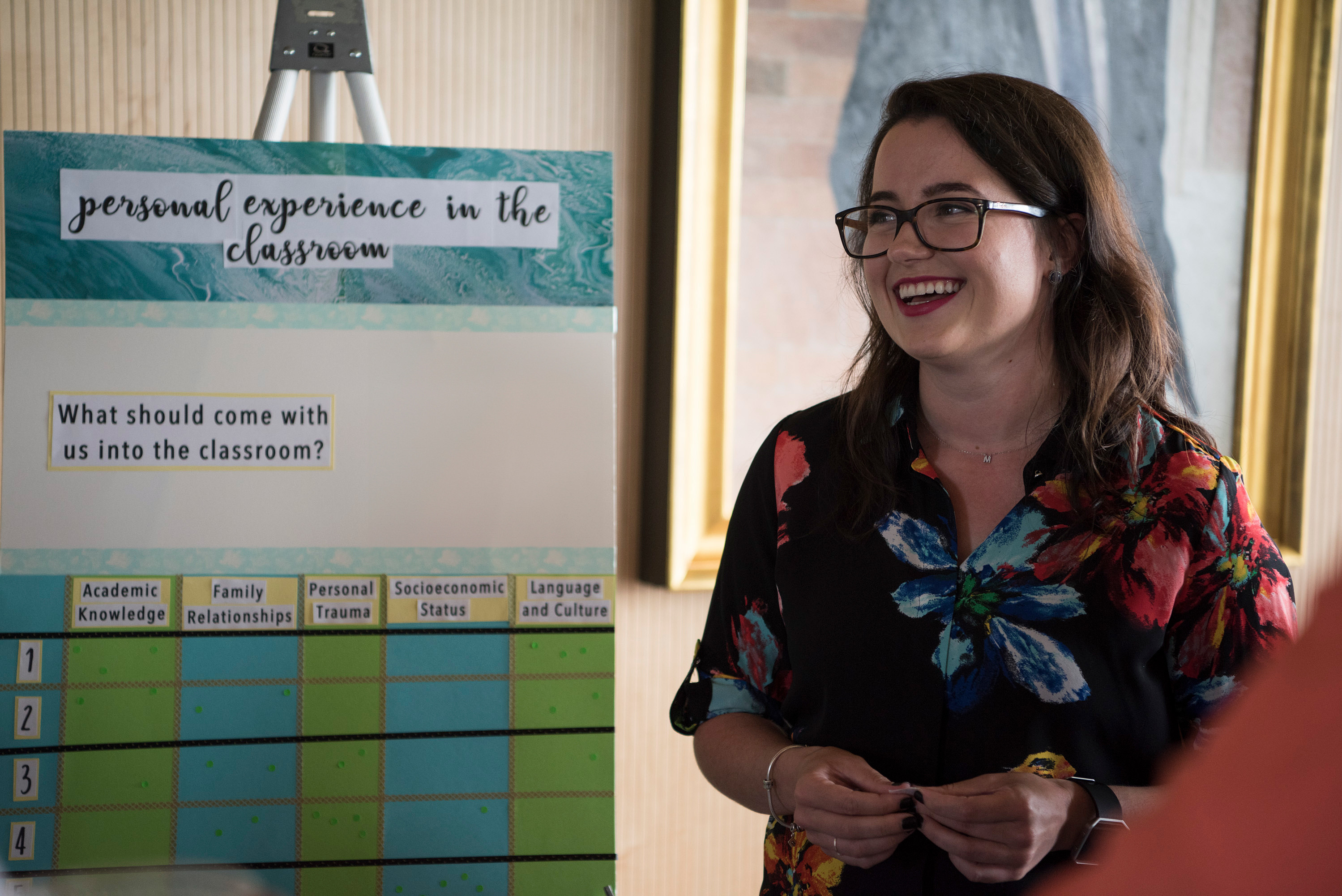 A woman in glasses stands next to a poster board.