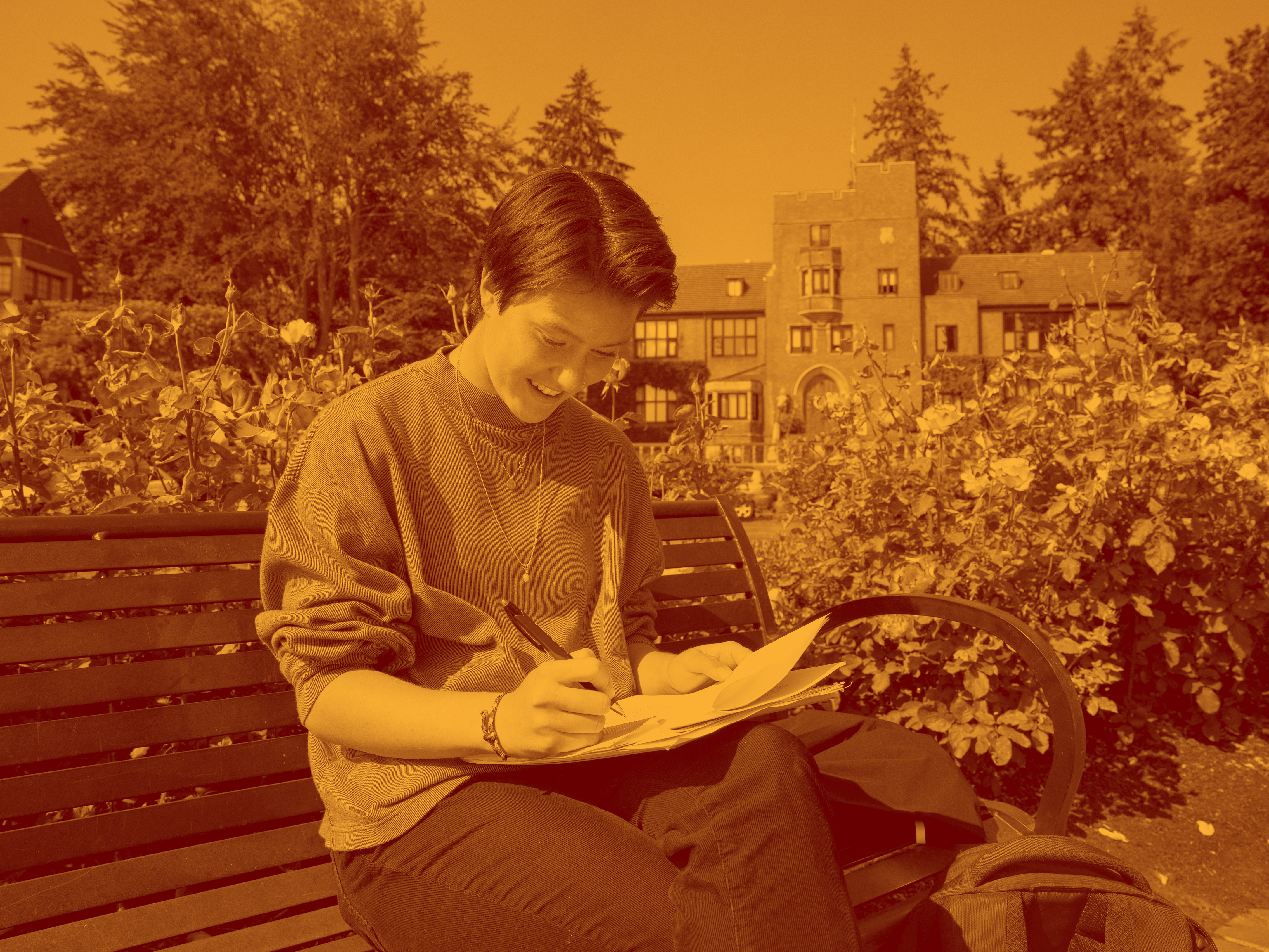 Maroon and yellow tonal image of a student sitting and taking notes outside.
