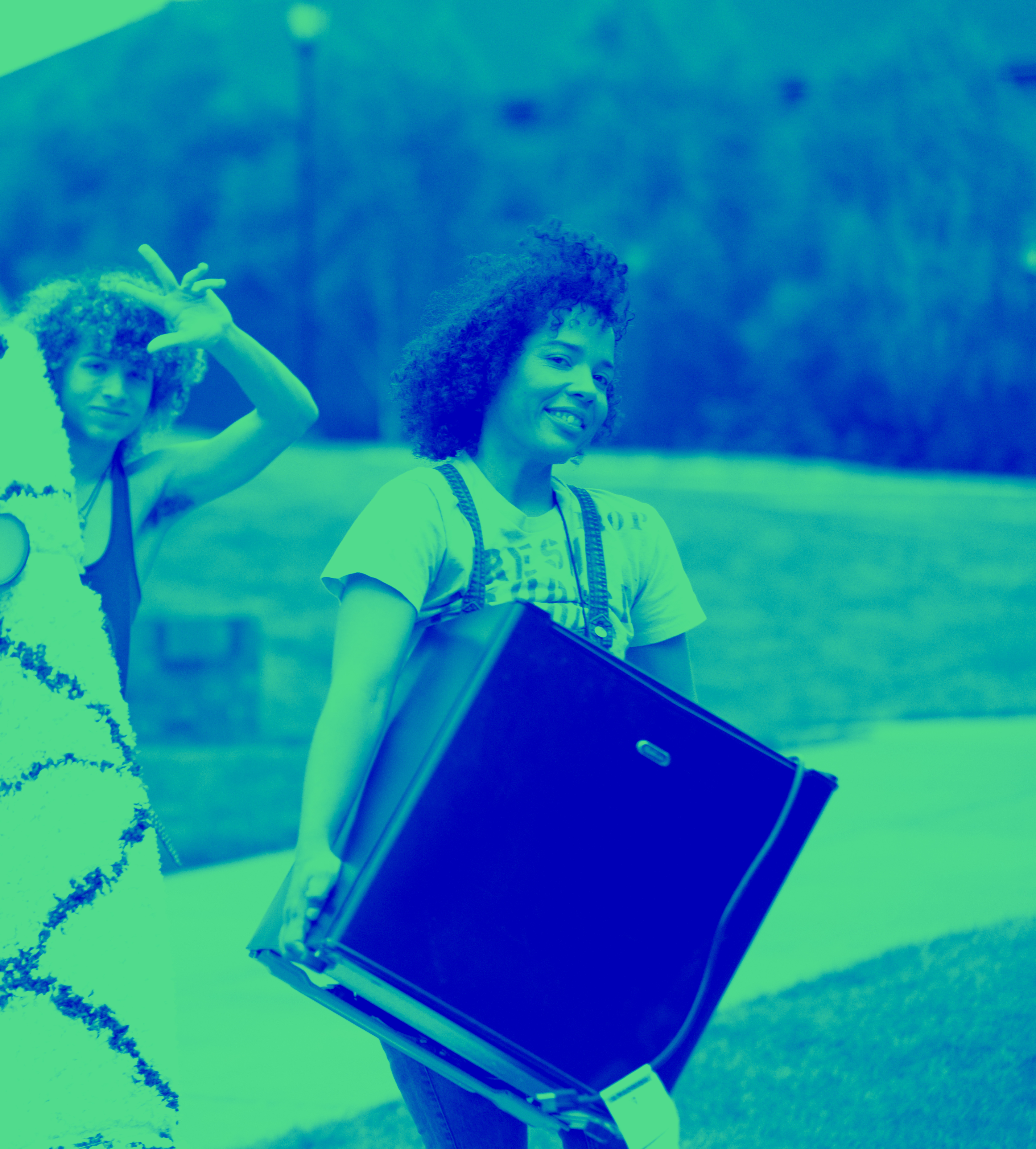 Blue and green tonal image of a student holding a mini fridge smiling at the camera.