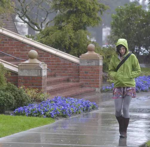 A student in a green raincoat walks near Jones Hall in the rain.