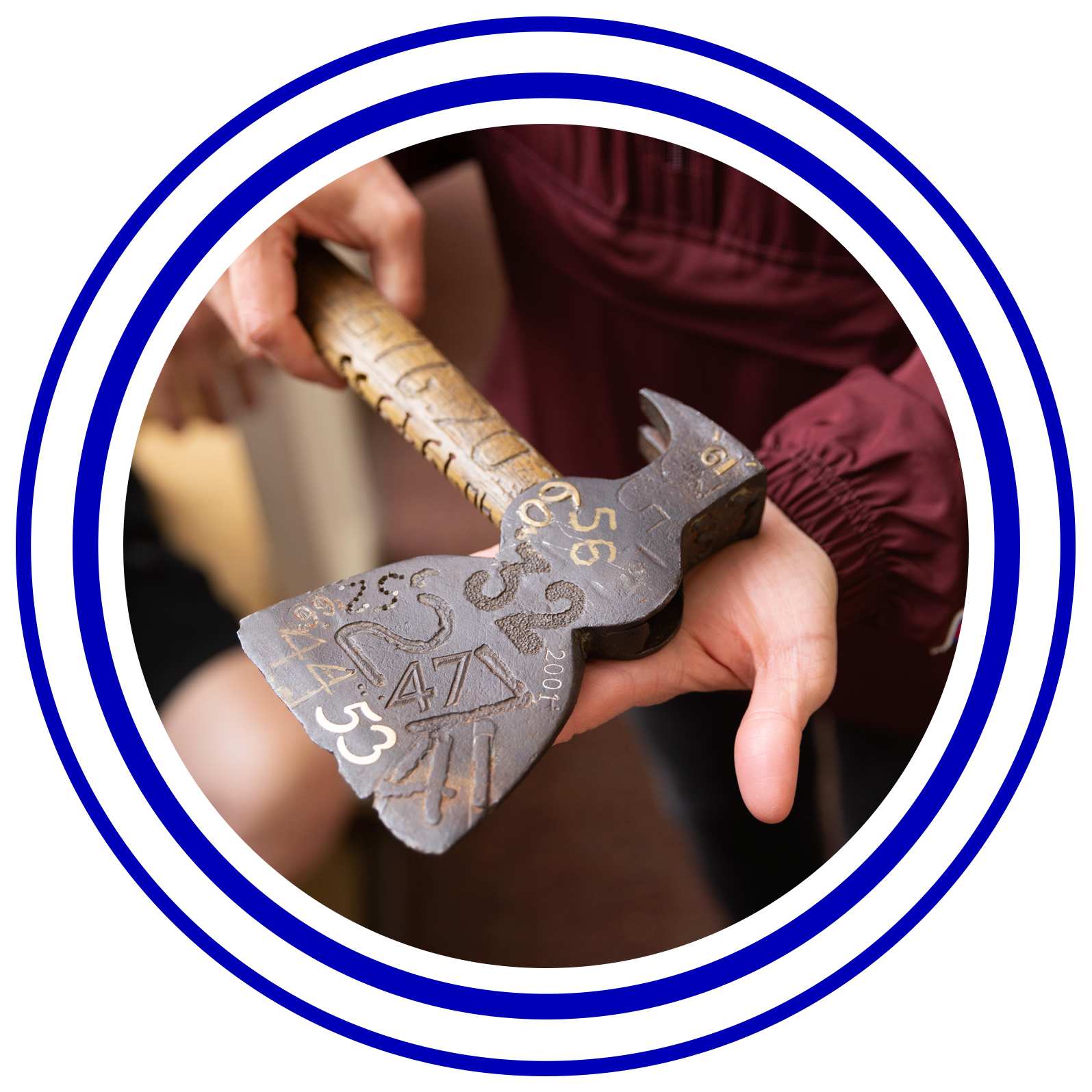 Circular image with colorful rings around it of someone holding a hatchet with year engraved on it.