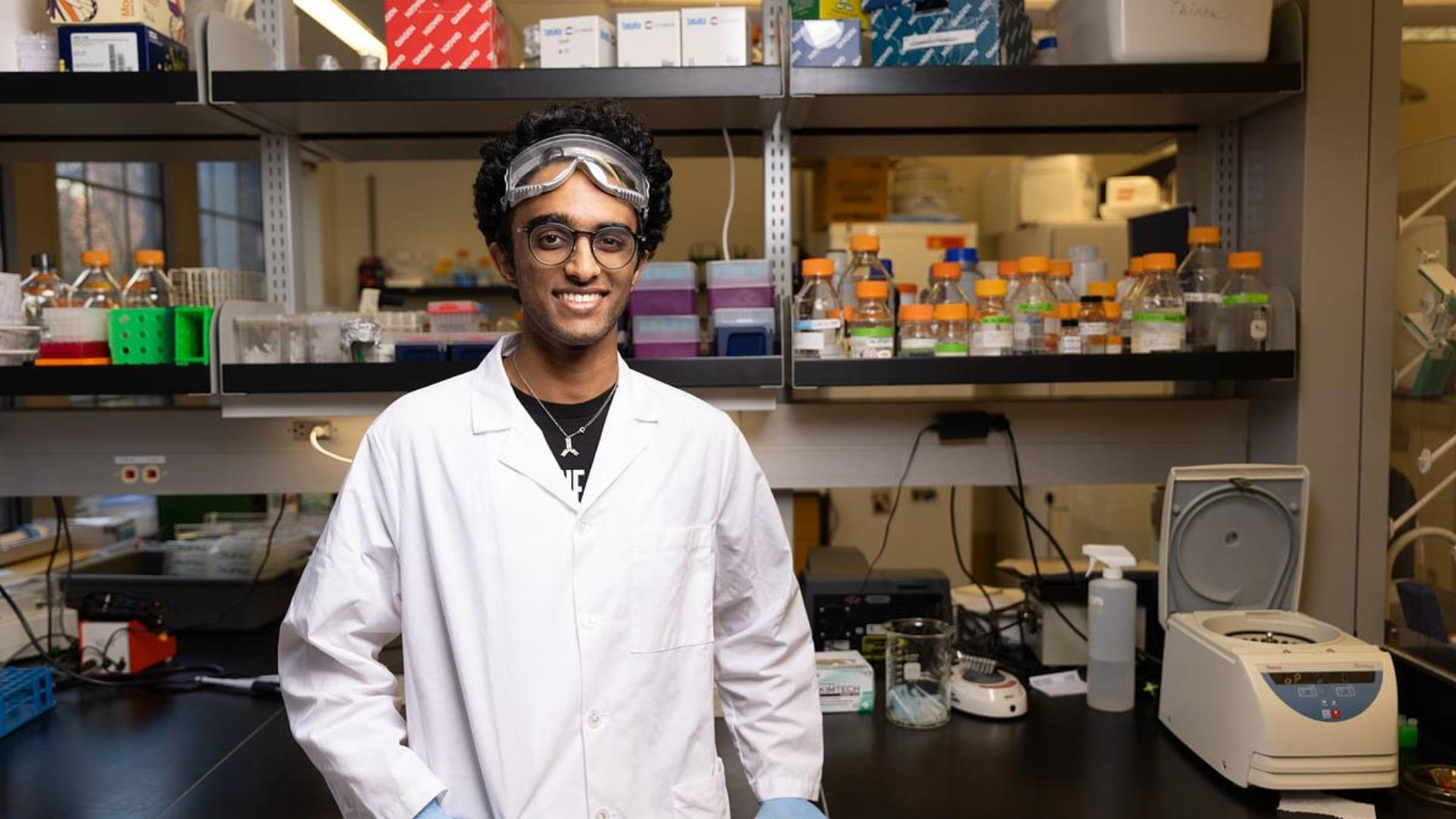 A student in a labcoat and goggles in the lab.
