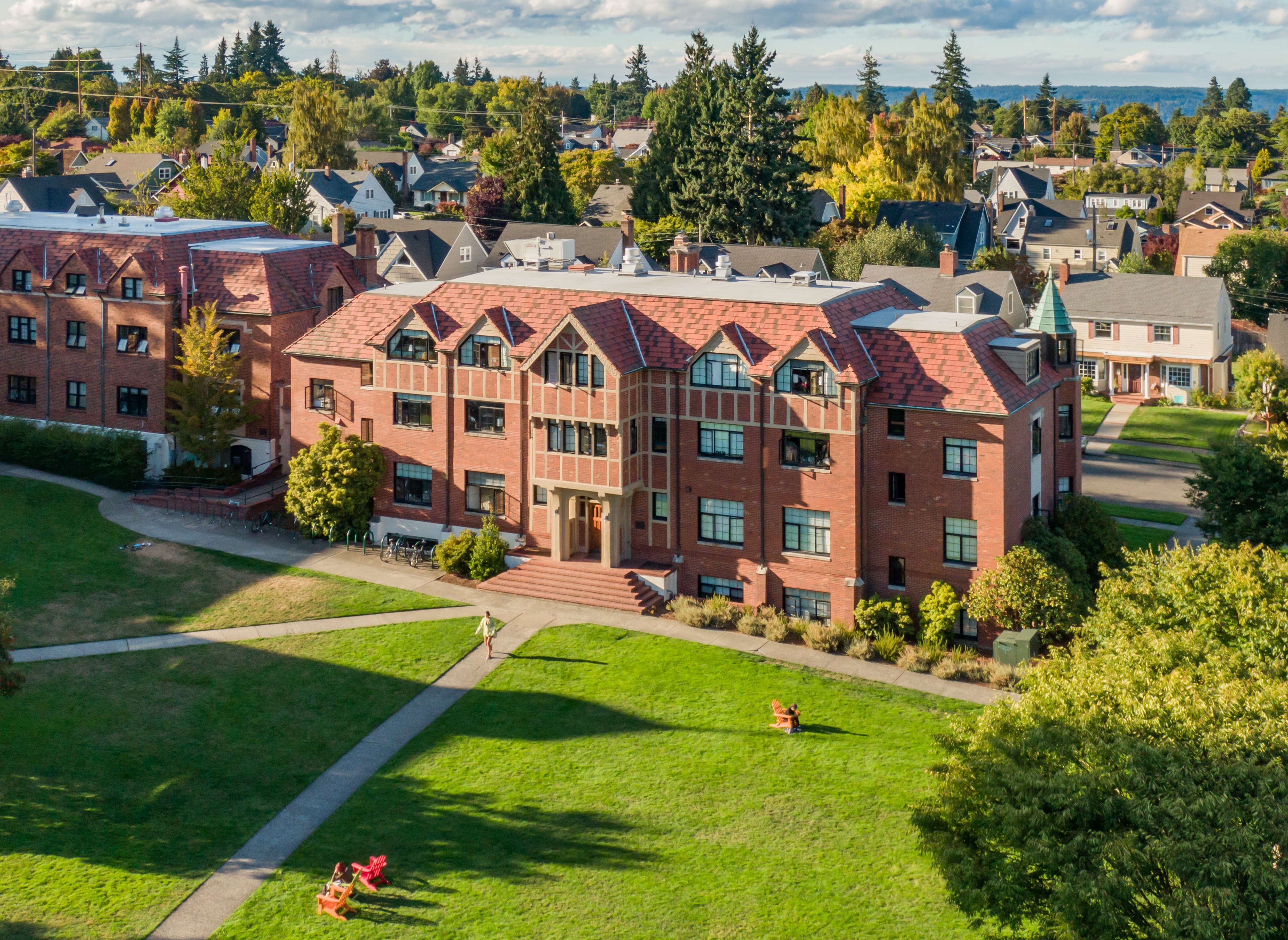Image of red brick buildings with lawn in front and evergreens and horizon line behind