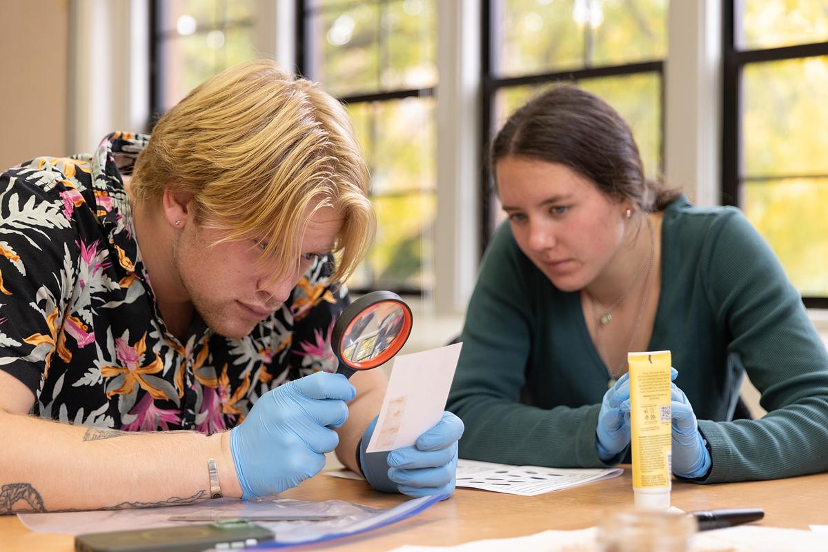Student inspects a piece of paper with a magnifying glass. 