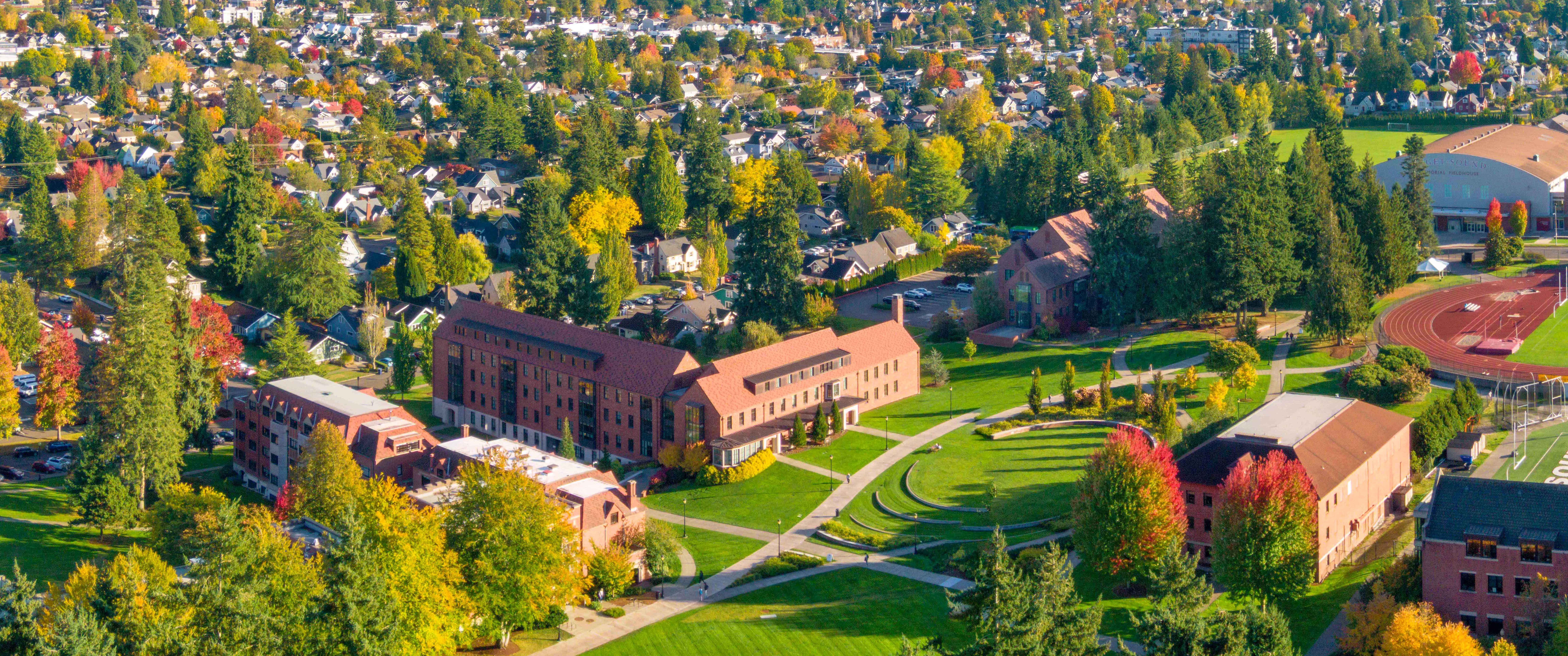 Aerial image of campus with red brick buildings, green lawns, and evergreens in the foreground.