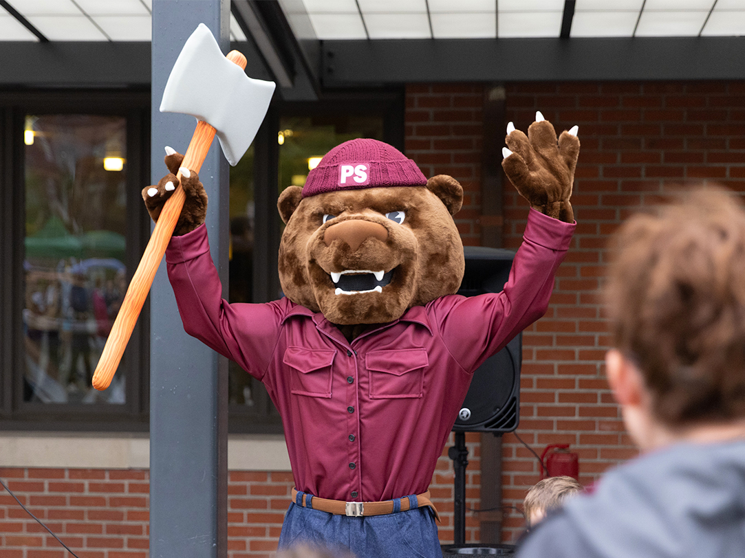 Grizzly bear mascot holding an axe with his hands in the air.
