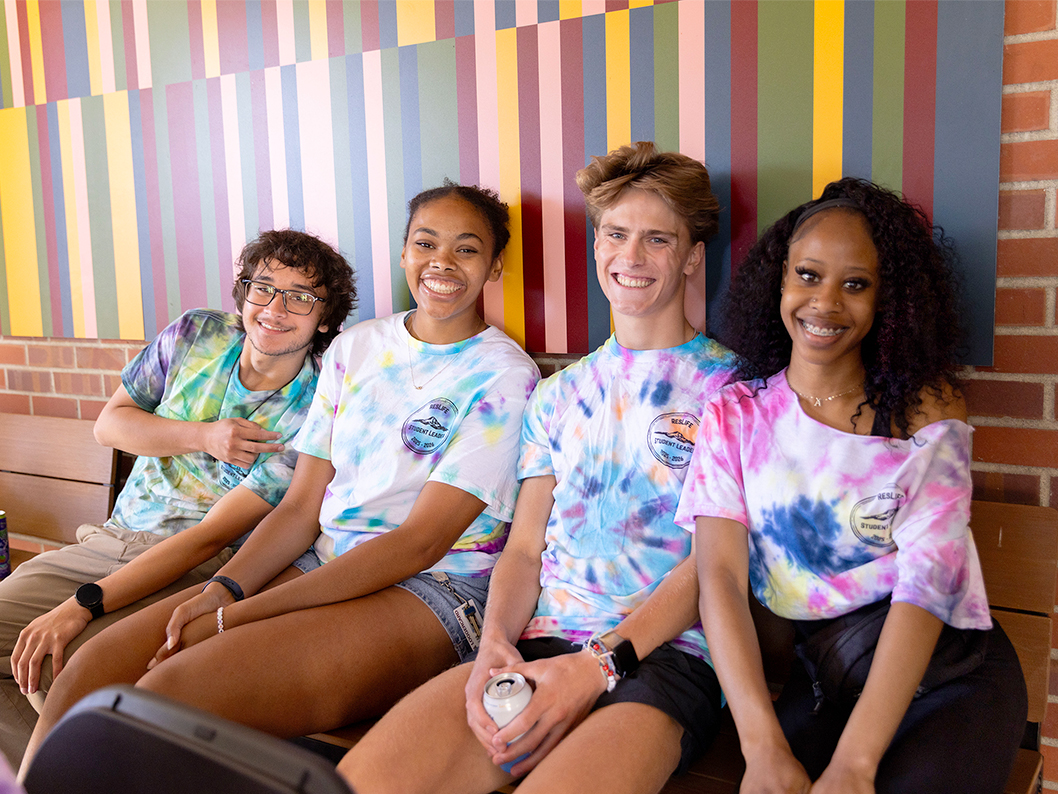 Four students in tie dye sitting and smiling at the camera.