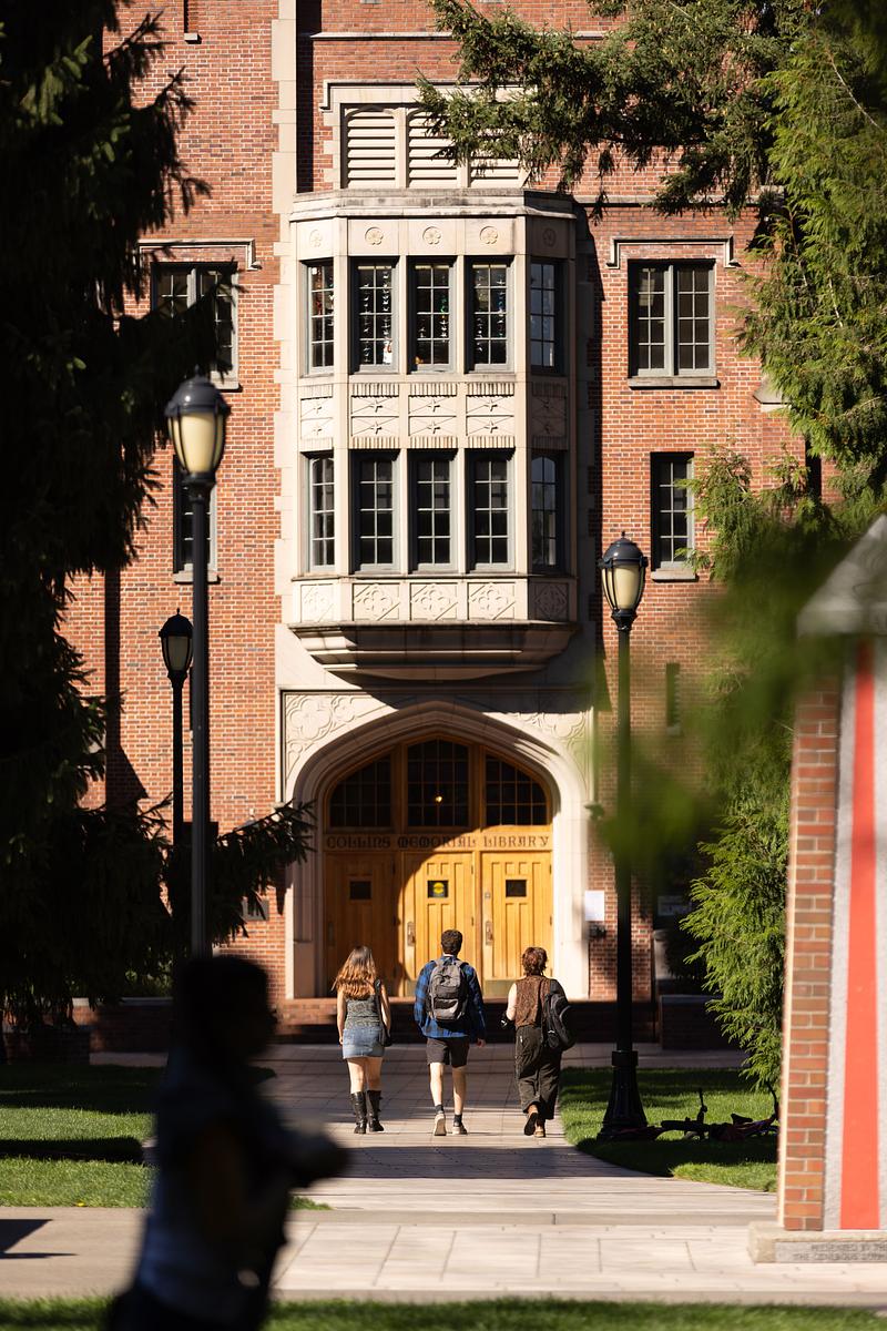 Three students walk toward a red brick building.