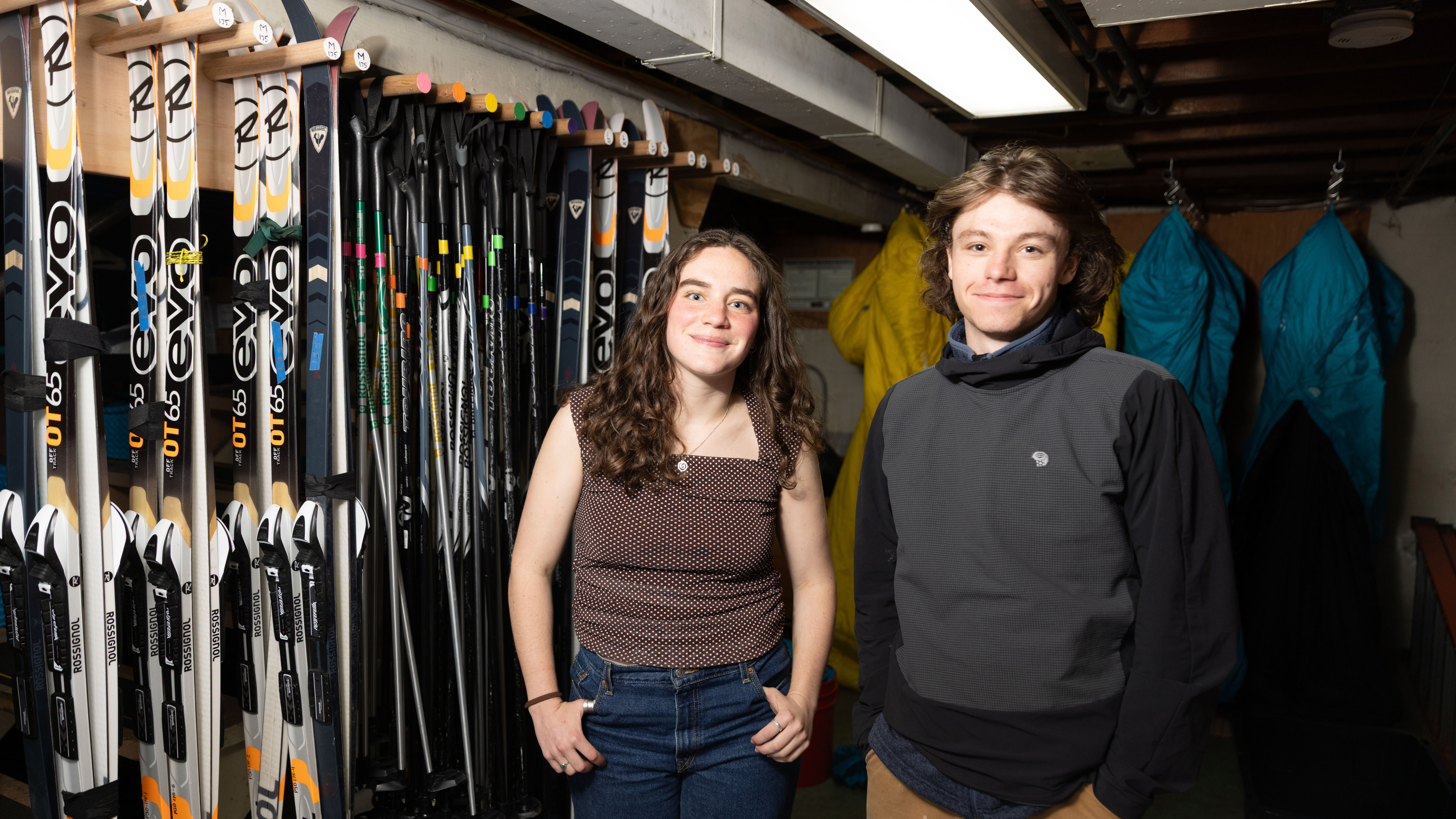 Claire Bargman ’26 and Reggie Westgate ’27 in front of a row of skis at the Expeditionary.
