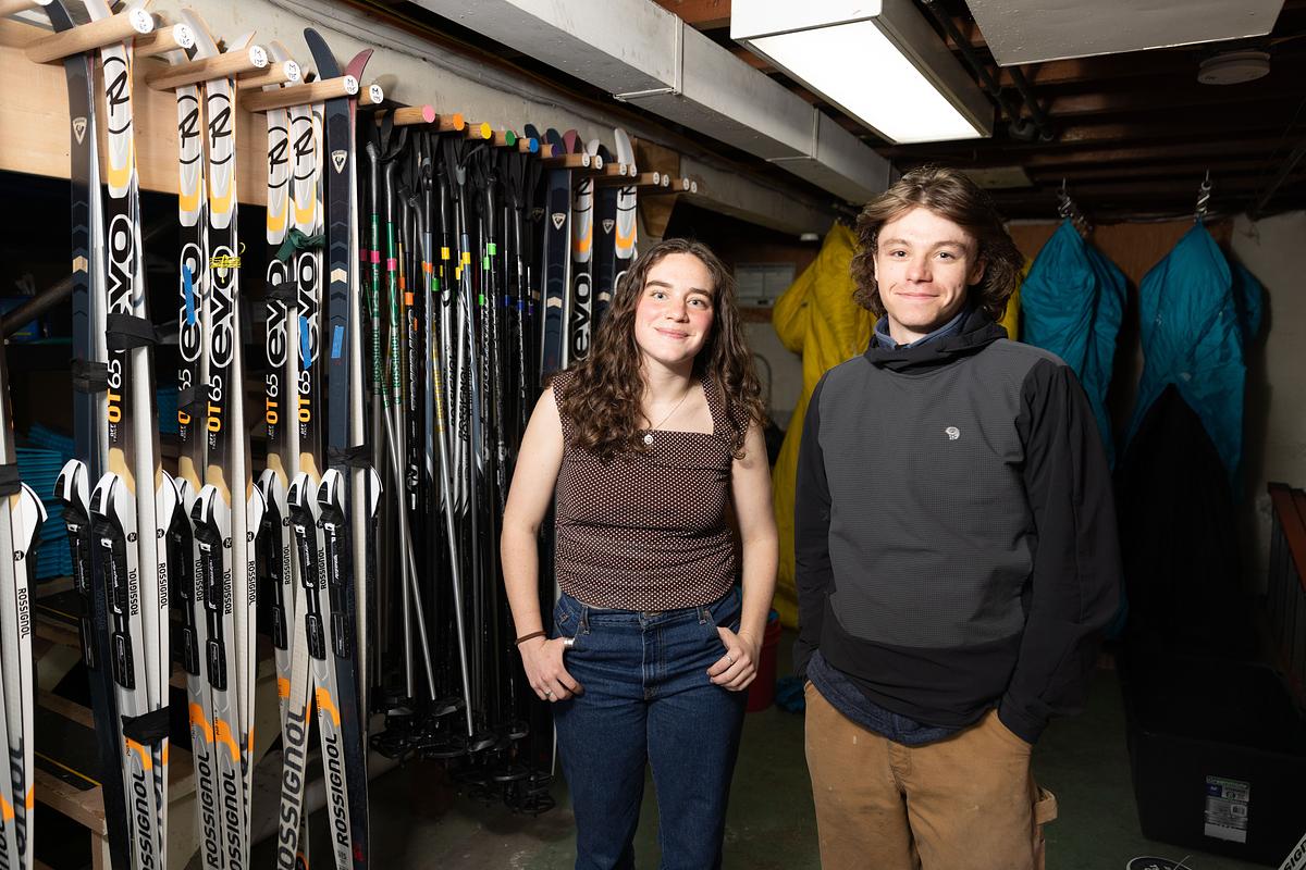 Claire Bargman ’26 and Reggie Westgate ’27 in front of a row of skis at the Expeditionary.
