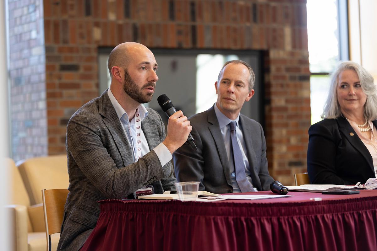 Two men and a woman sit at a table speaking to an audience.