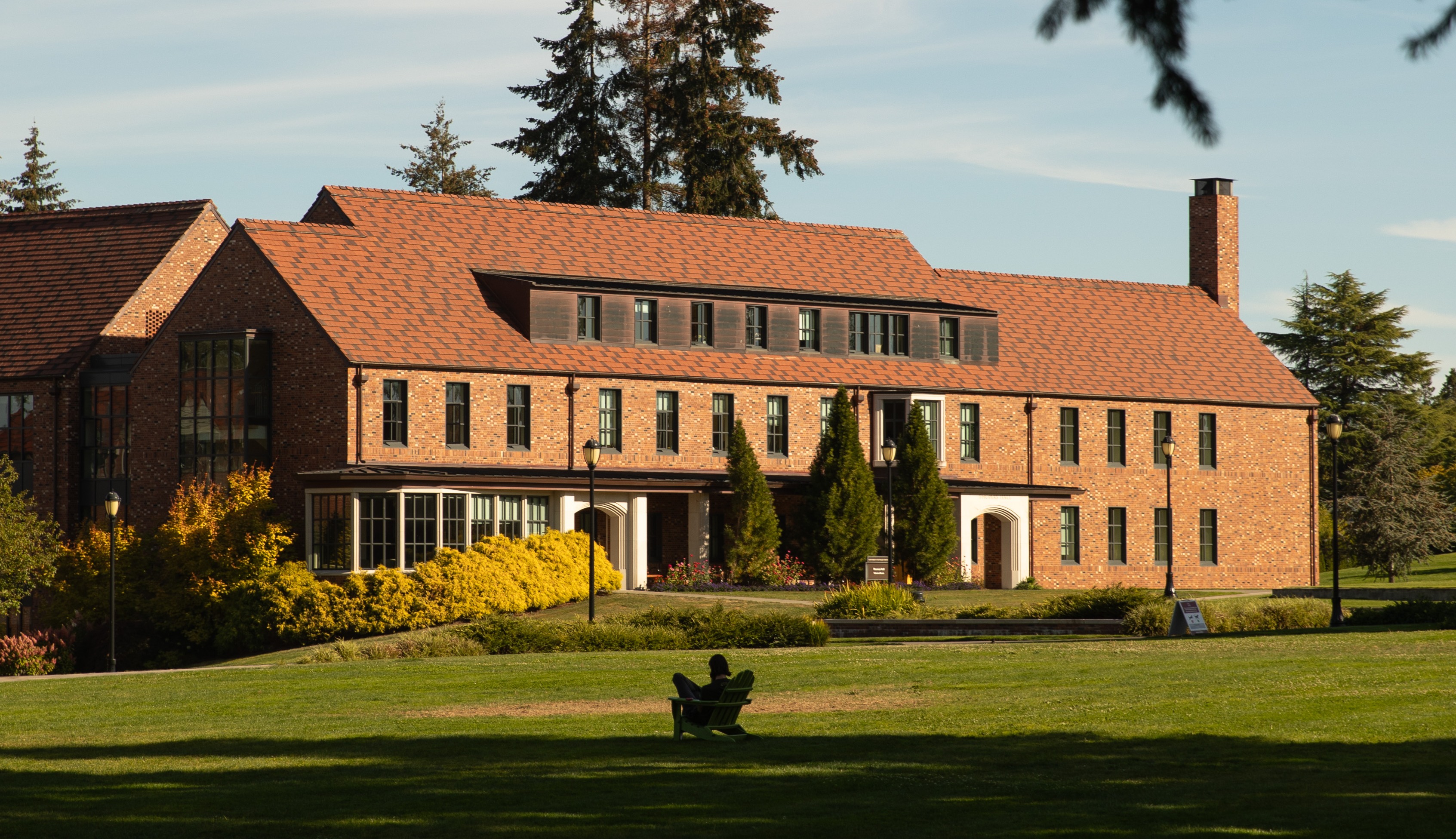 Student sits in an Adirondack chair on Todd Field in front of Thomas Hall.