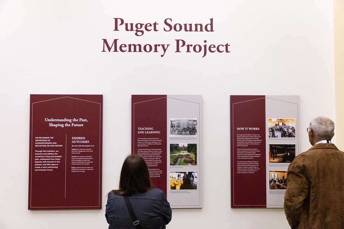 Two people view three large plaques with the title PUGET SOUND MEMORY PROJECT above them. 