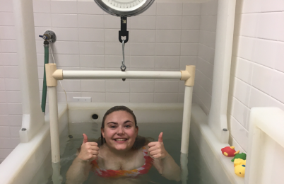 A person smiling and holding their thumbs up in water.