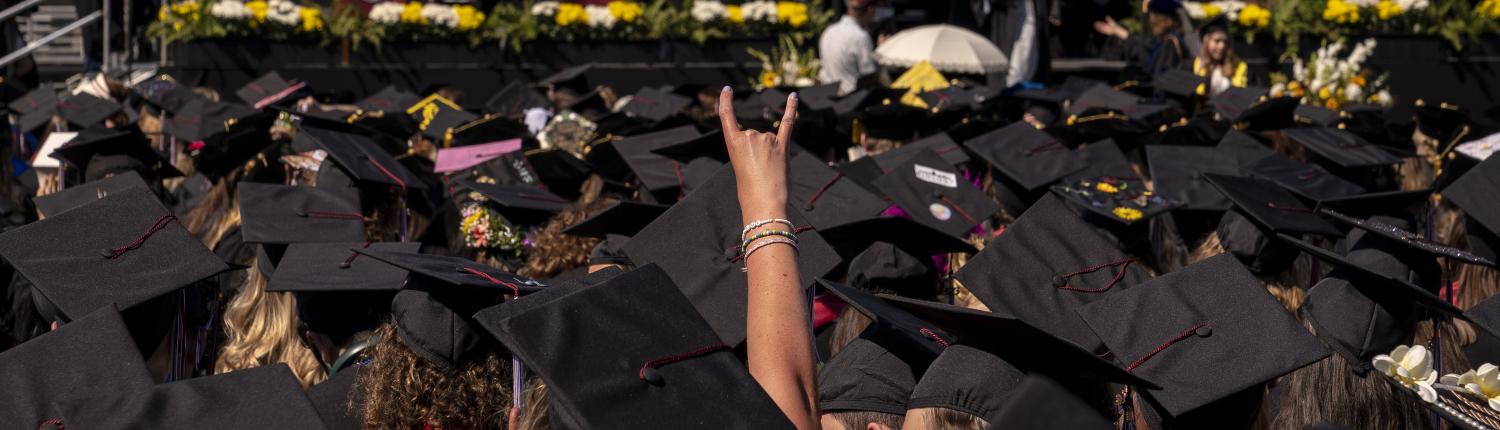 An arms shoots out above a dozen black mortar boards at a graduation ceremony. 