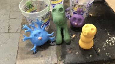 Blue, green, purple, and yellow claymation figures sit on the corner of a work table