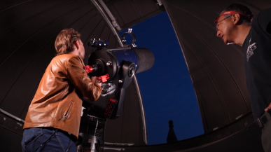 Austin Glock and Visiting Asst. Prof. Tanaka look up past the telescope into the starry sky outside the observatory dome.
