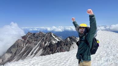 A PacTrail student raises their hands in victory at the summit of Mount St. Helens.