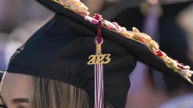 A black mortar board sits on top of a women's head with the 2023 medallion facing the camera. 