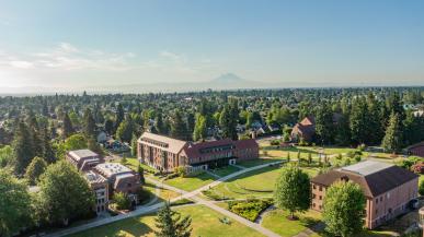 Image taken over campus with buildings below, trees stretched out to the horizon, and Mount Rainier in the distance.