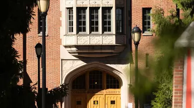 Three students walk toward a red brick building.