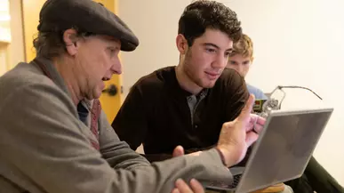Prof. Neshyba points to a laptop screen while a student looks on. 