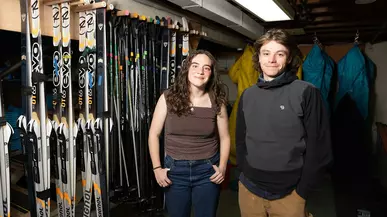 Claire Bargman ’26 and Reggie Westgate ’27 in front of a row of skis at the Expeditionary.