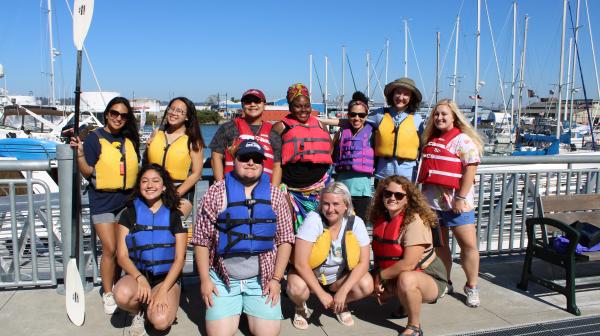A group of students in life vest stand on a dock smile at the camera.