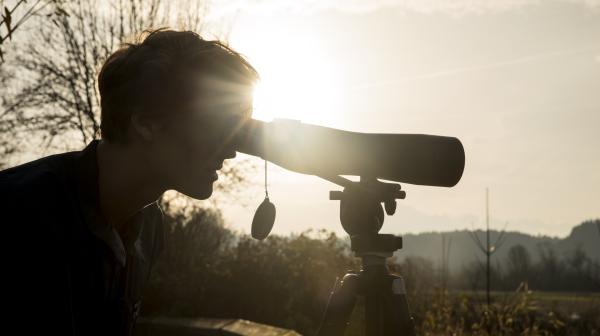 A silhouetted person looks through a telescope.