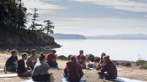 Students sit in a circle on yoga mats with the Puget Sound in the background.