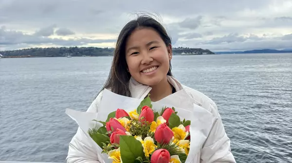 a girl holding flowers with water in the background