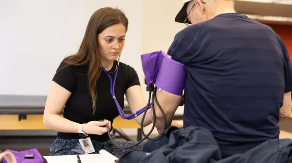 graduate student taking blood pressure of patient facing them, sitting on a PT table