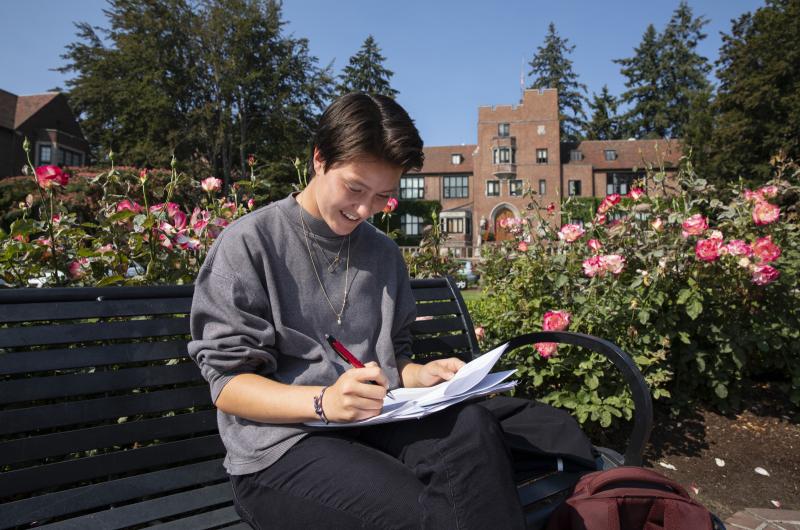 A student works on homework while sitting on a bench near the fountain in Jones Circle.